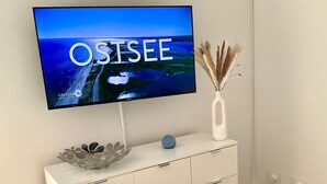 A flat-screen TV mounted on a white cabinet with a decorative bowl and a vase with dried plants. - Vacation apartment small quiet oasis - forest edge location, central in Scharbeutz - House (Scharbeutz)