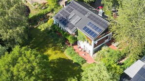 An aerial view of a modern house with solar panels on the roof, surrounded by lush greenery. - Vacation apartment small quiet oasis - forest edge location, central in Scharbeutz - House (Scharbeutz)