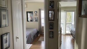 A hallway leading to a bedroom with a bed, framed pictures on the walls, and a view of a balcony with outdoor furniture. - FIRST FLOOR FLAT FOR BUSINESS OR PLEASURE (Buffalo)
