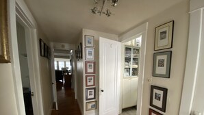 A hallway with wooden flooring, white walls, and multiple framed pictures. There is a door leading to a room with a cabinet and a mirror. - FIRST FLOOR FLAT FOR BUSINESS OR PLEASURE (Buffalo)