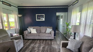 Una sala de estar con una pared azul oscuro de acento, un sofá gris con cojines estampados, piso de madera y una lámpara.
