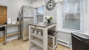 Une cuisine moderne avec un réfrigérateur en acier inoxydable, une table blanche avec un banc et une horloge au mur.