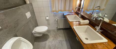 A modern bathroom with a toilet, bidet, and two sinks with mirrors.