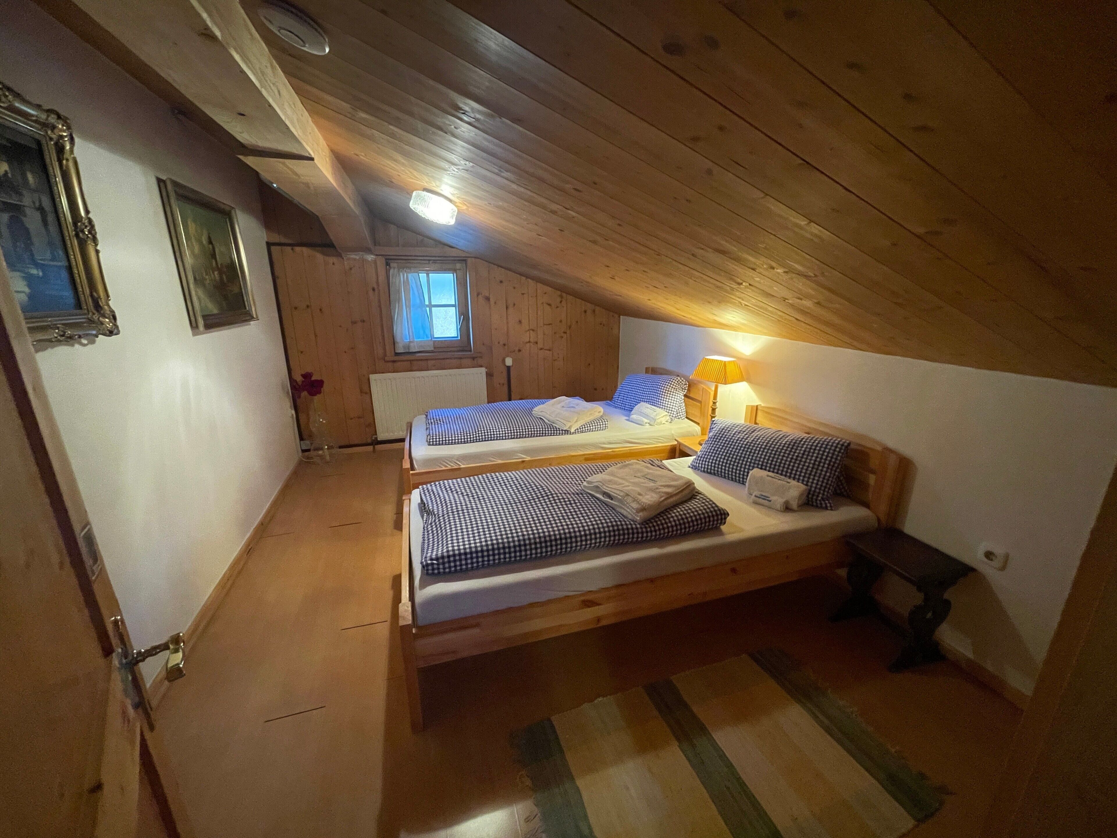 Une pièce avec des poutres en bois, deux lits avec une literie à carreaux, une fenêtre donnant sur un paysage agréable et un radiateur.