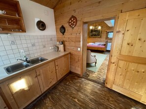 L’intérieur est en bois et comprend un coin cuisine équipé d’un évier, de placards et d’un plan de travail. On aperçoit un lit avec une fenêtre en arrière-plan.
