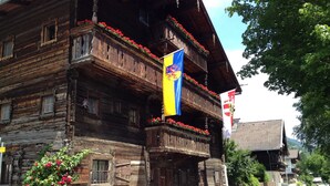Un edificio de madera tradicional con balcones, zócalo de piedra y banderas.