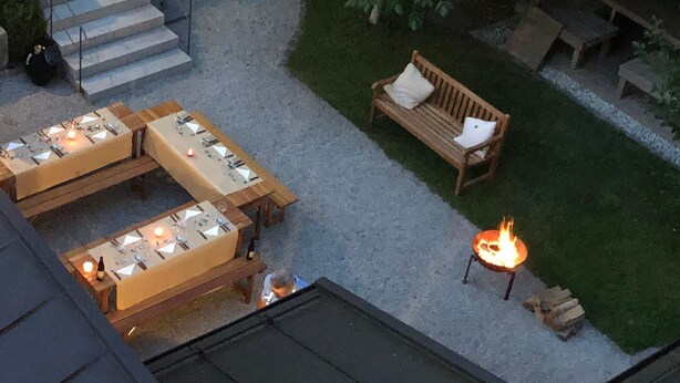 Un patio al aire libre con mesas, sillas, una fogata y un banco de madera.