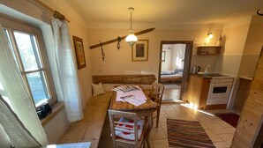 Una habitación acogedora con una mesa de madera, sillas, ventilador de techo, ventana con cortinas, cama y kitchenette.