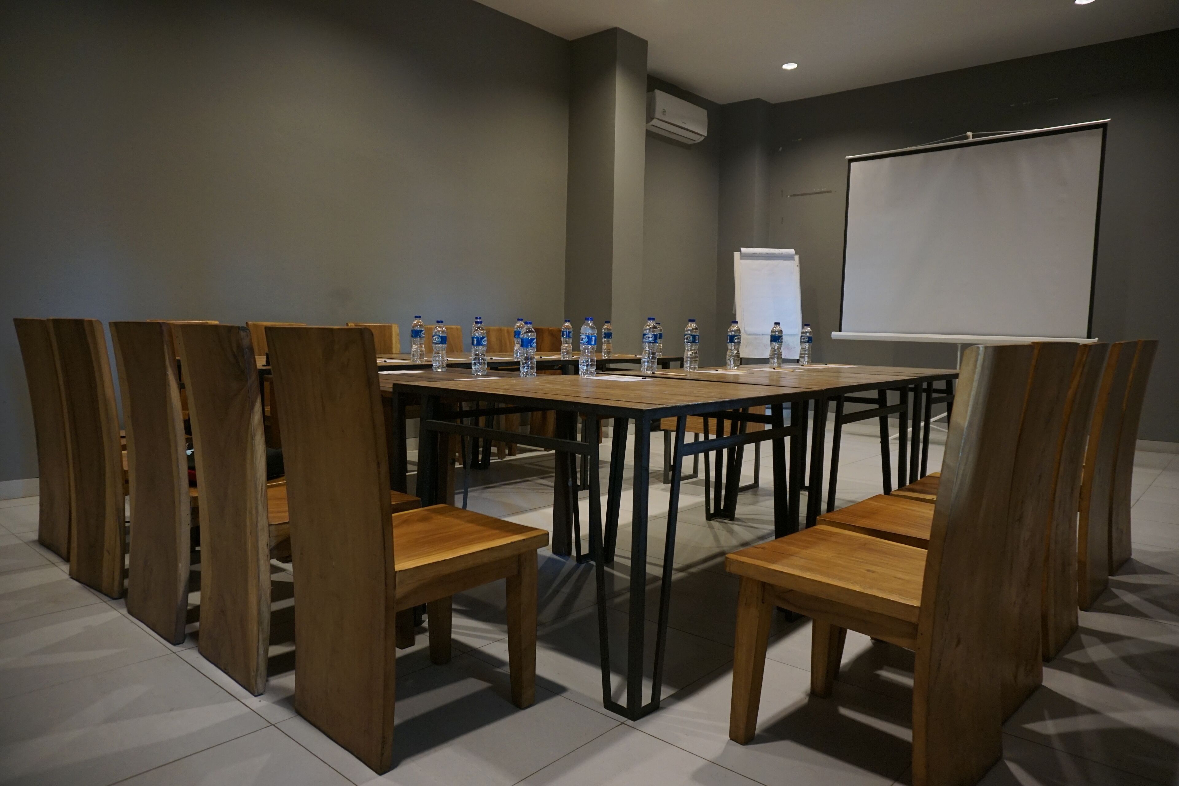 Sala de conferências com uma mesa comprida, cadeiras de madeira e garrafas de água.