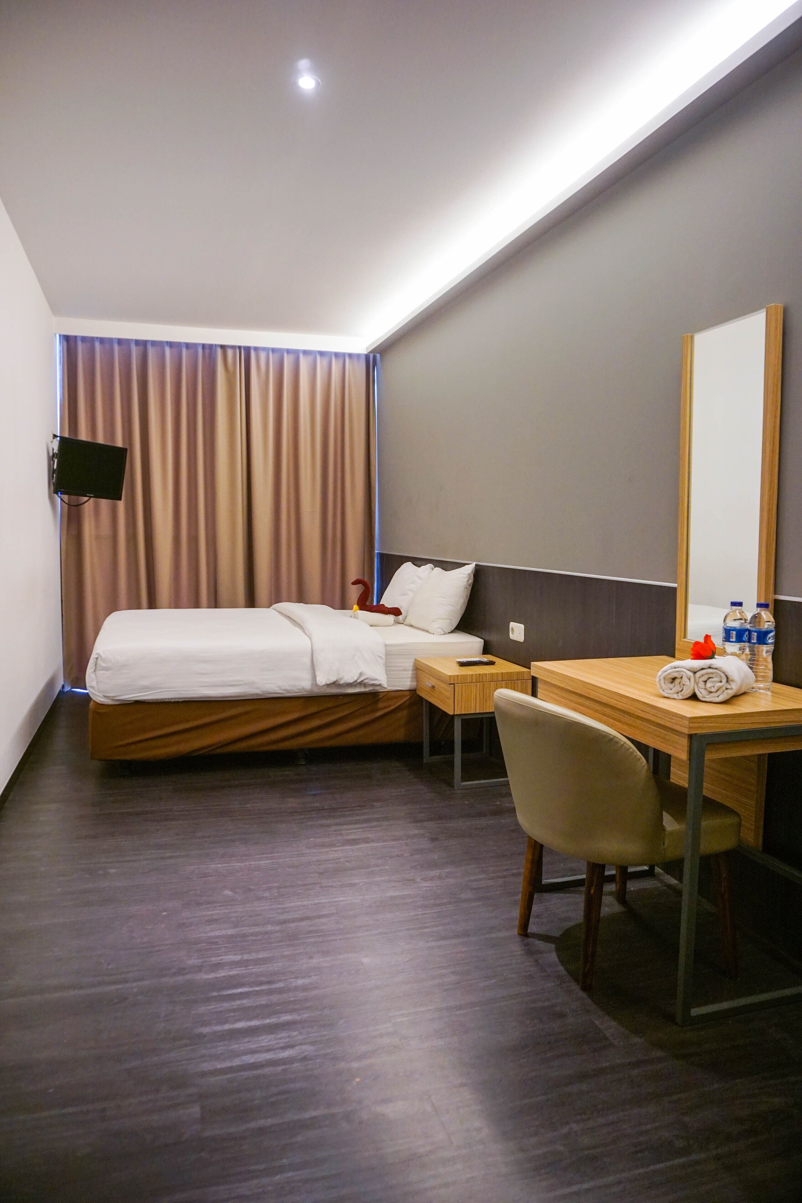 Habitación de hotel con cama, escritorio, silla, televisor de pantalla plana, espejo y ventana con cortinas.