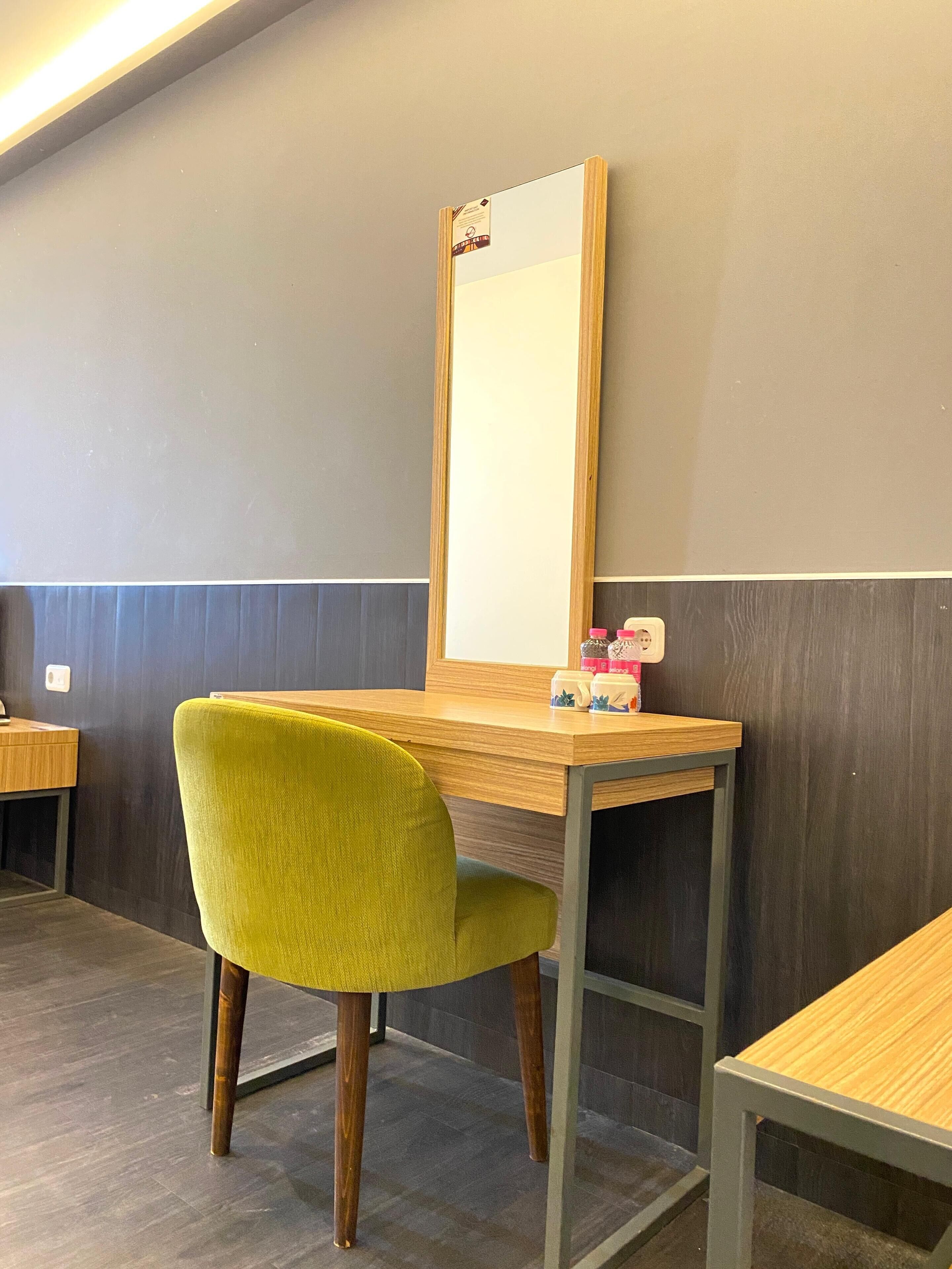A room with a wooden desk, a green chair, and a mirror on the wall.
