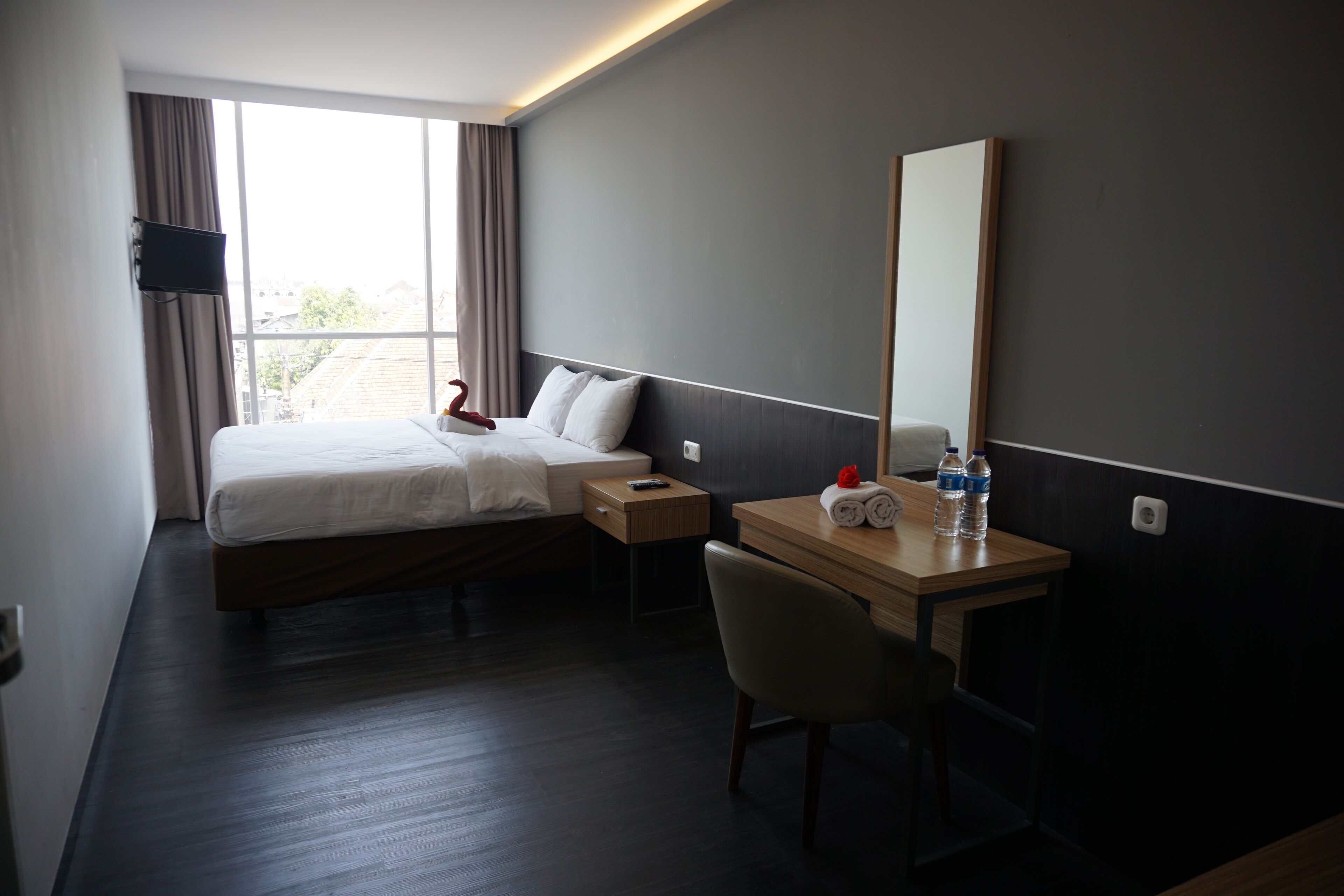 Ett hotellrum med en säng, ett nattduksbord, en stol, ett skrivbord och en stor spegel.