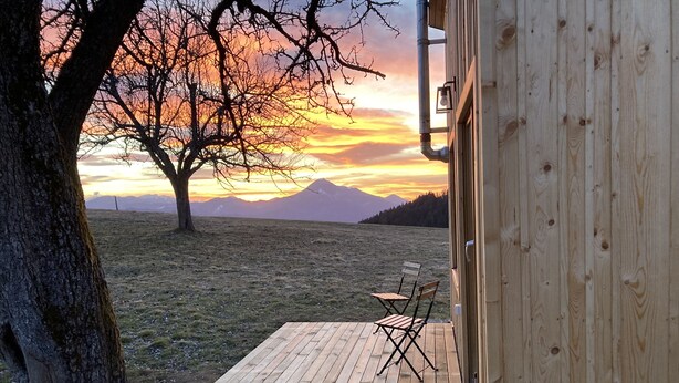 Une terrasse en bois offrant une vue sur le coucher de soleil et les montagnes.