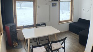 Une pièce avec un plafond en bois, une table blanche avec des chaises, un canapé noir et une fenêtre donnant sur un paysage enneigé.