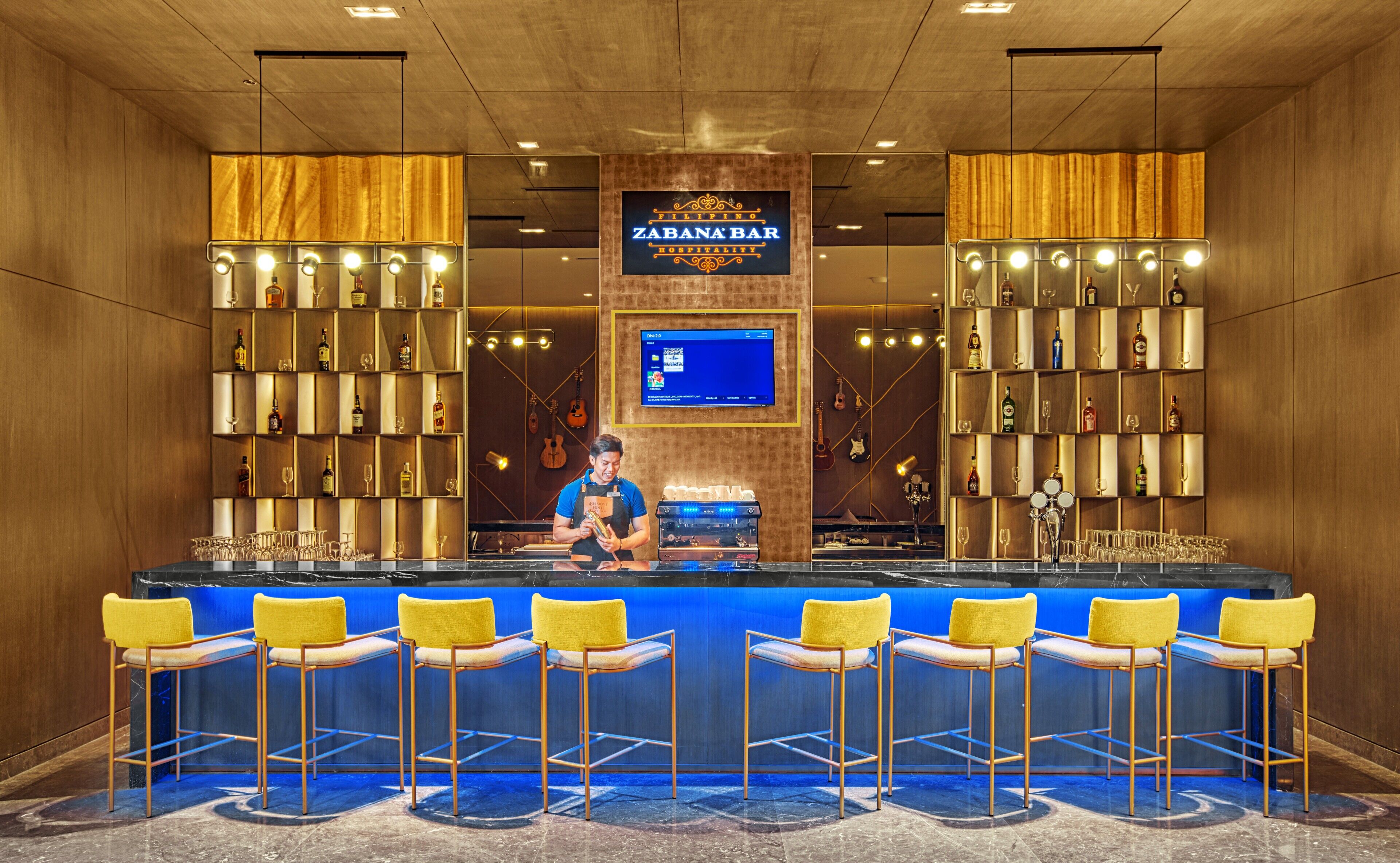A bar area with a bartender, shelves with bottles, and bar stools.