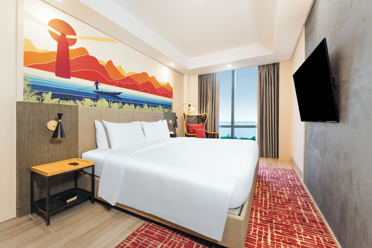 Een hotelkamer met een groot bed, een nachtkastje, een lamp, een televisie en uitzicht op de oceaan.