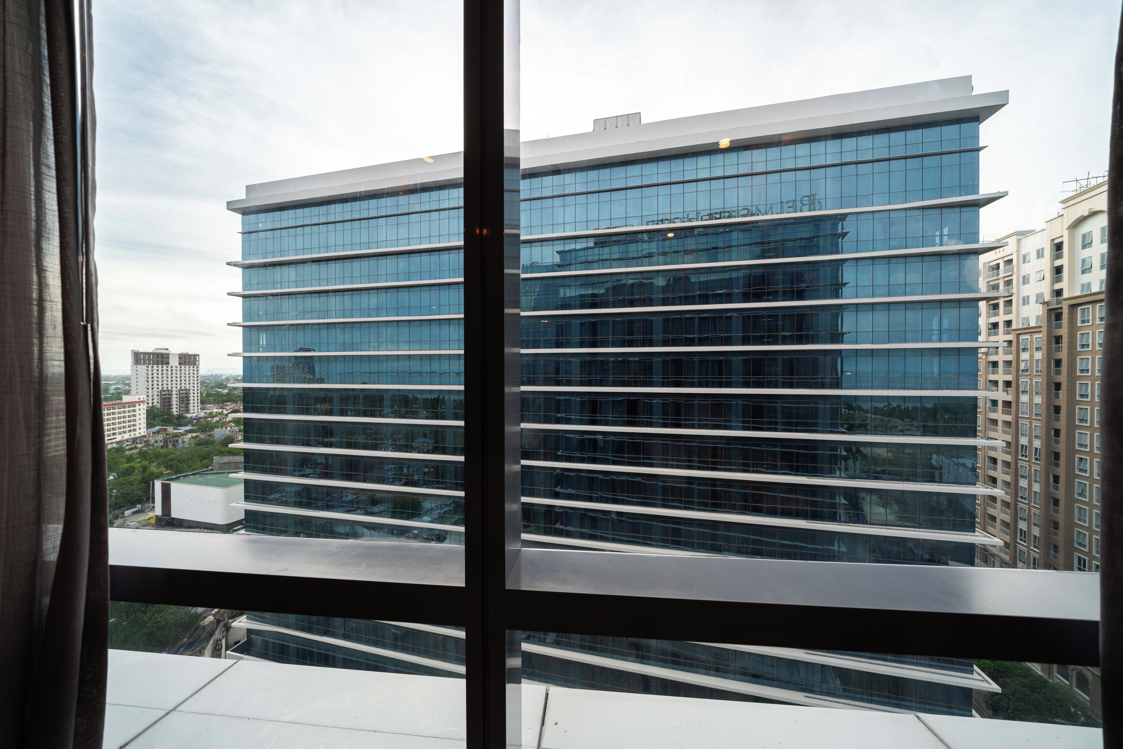 A multi-story building with a modern glass facade, viewed through a window with a metal frame.