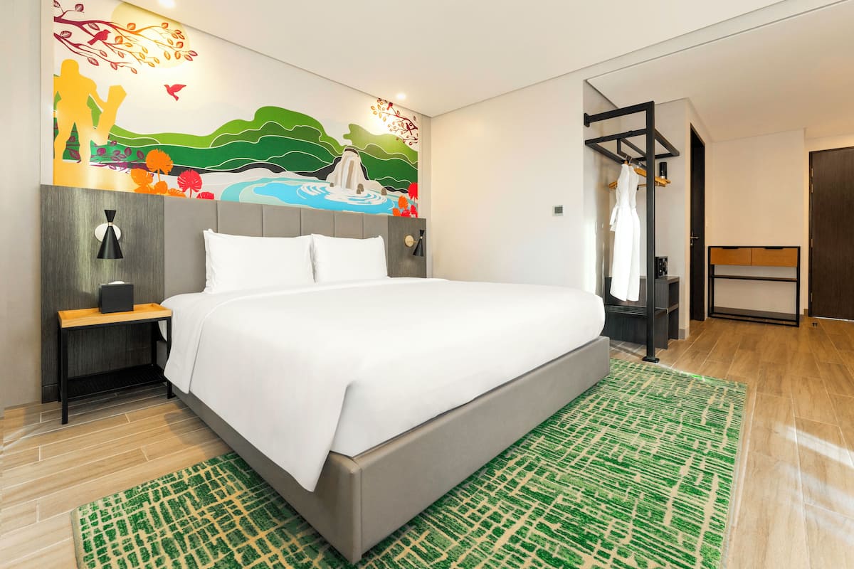 Een moderne hotelkamer met een groot bed, een nachtkastje, een wandplank en een groen vloerkleed met dessin.