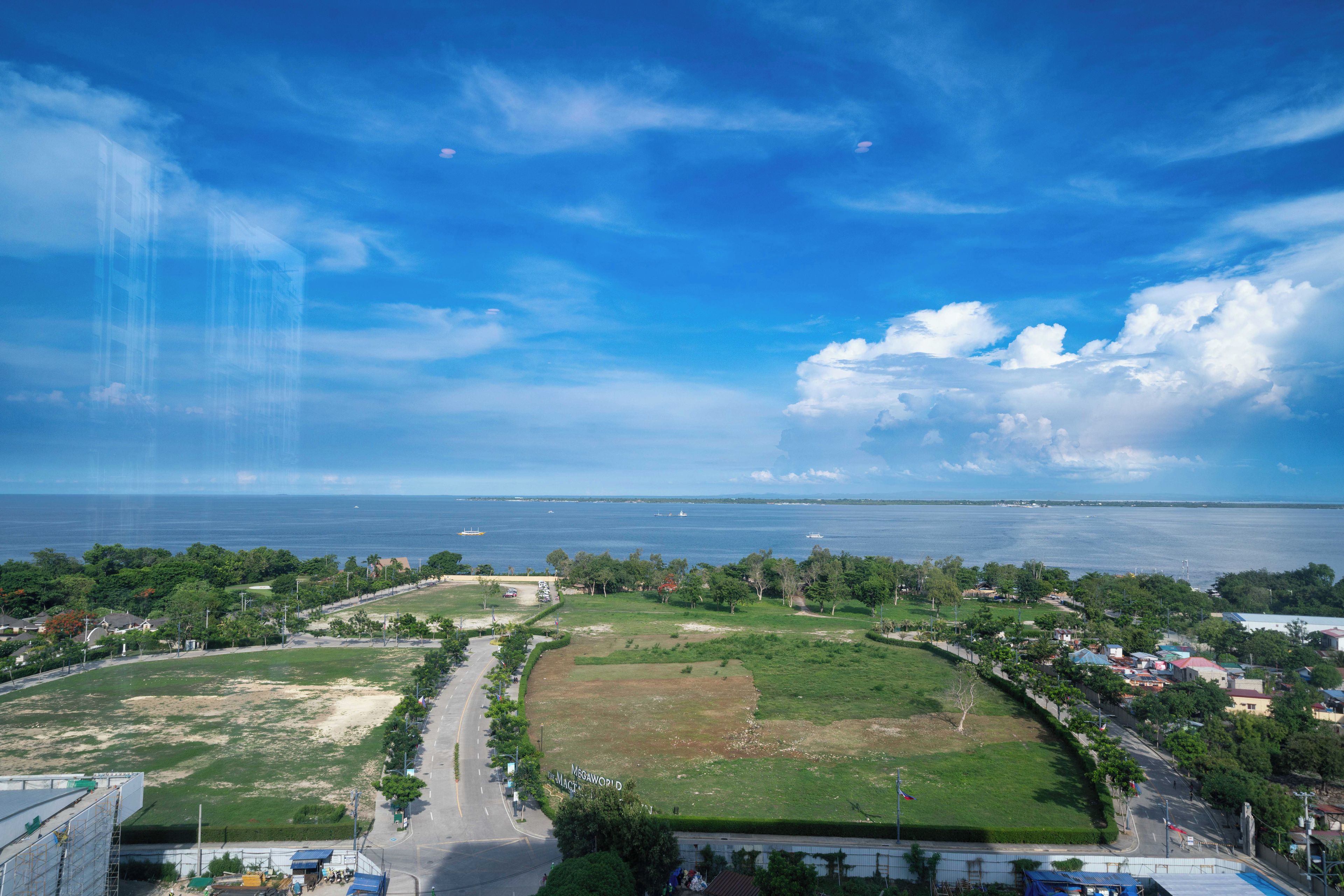 A coastal landscape with a clear sky, a large body of water, and a road leading to a building with a sign reading 'MEGAWORLD.'