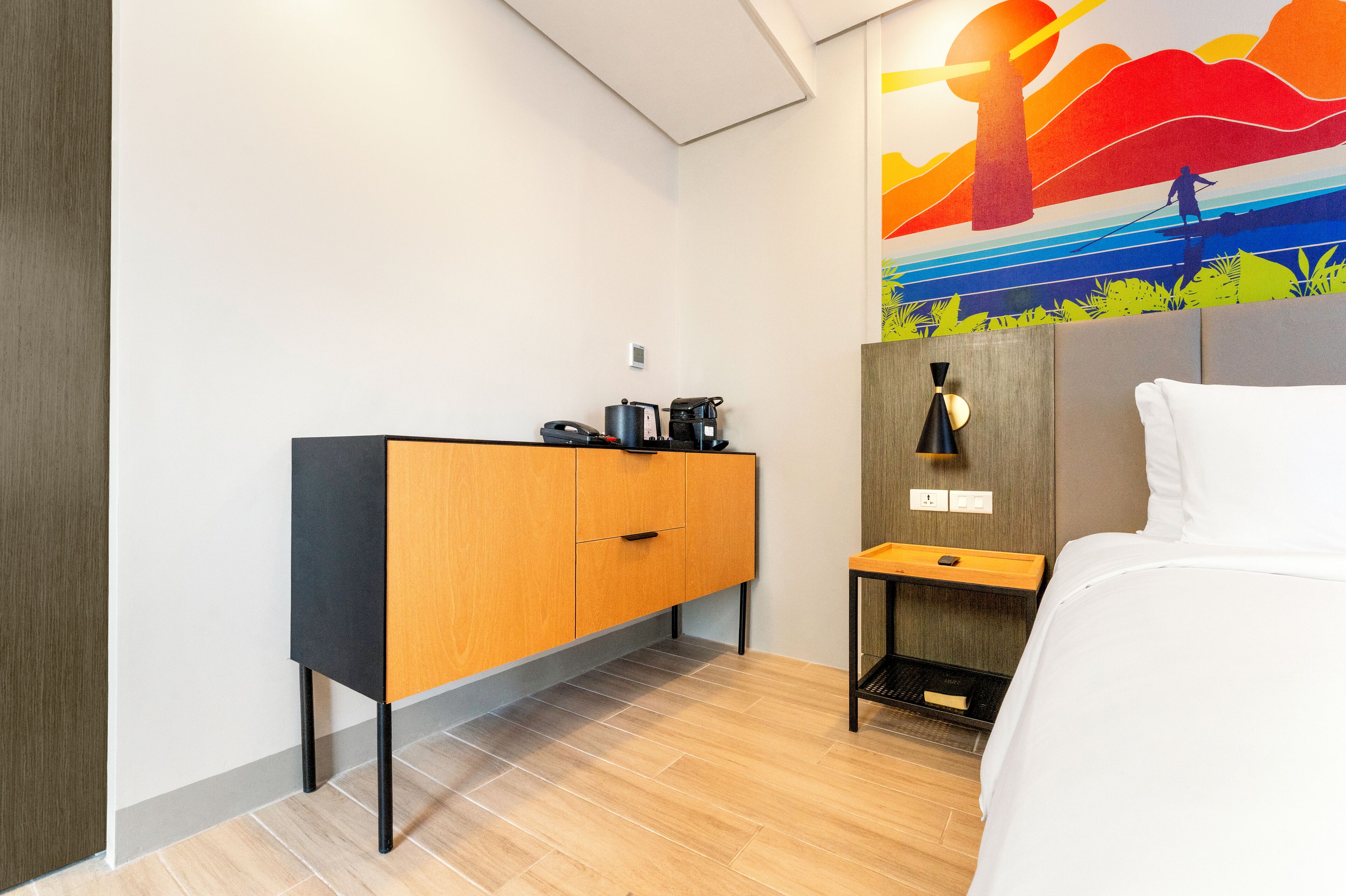 Een hotelkamer met een bed, een houten kast, een nachtkastje en een muurschildering.