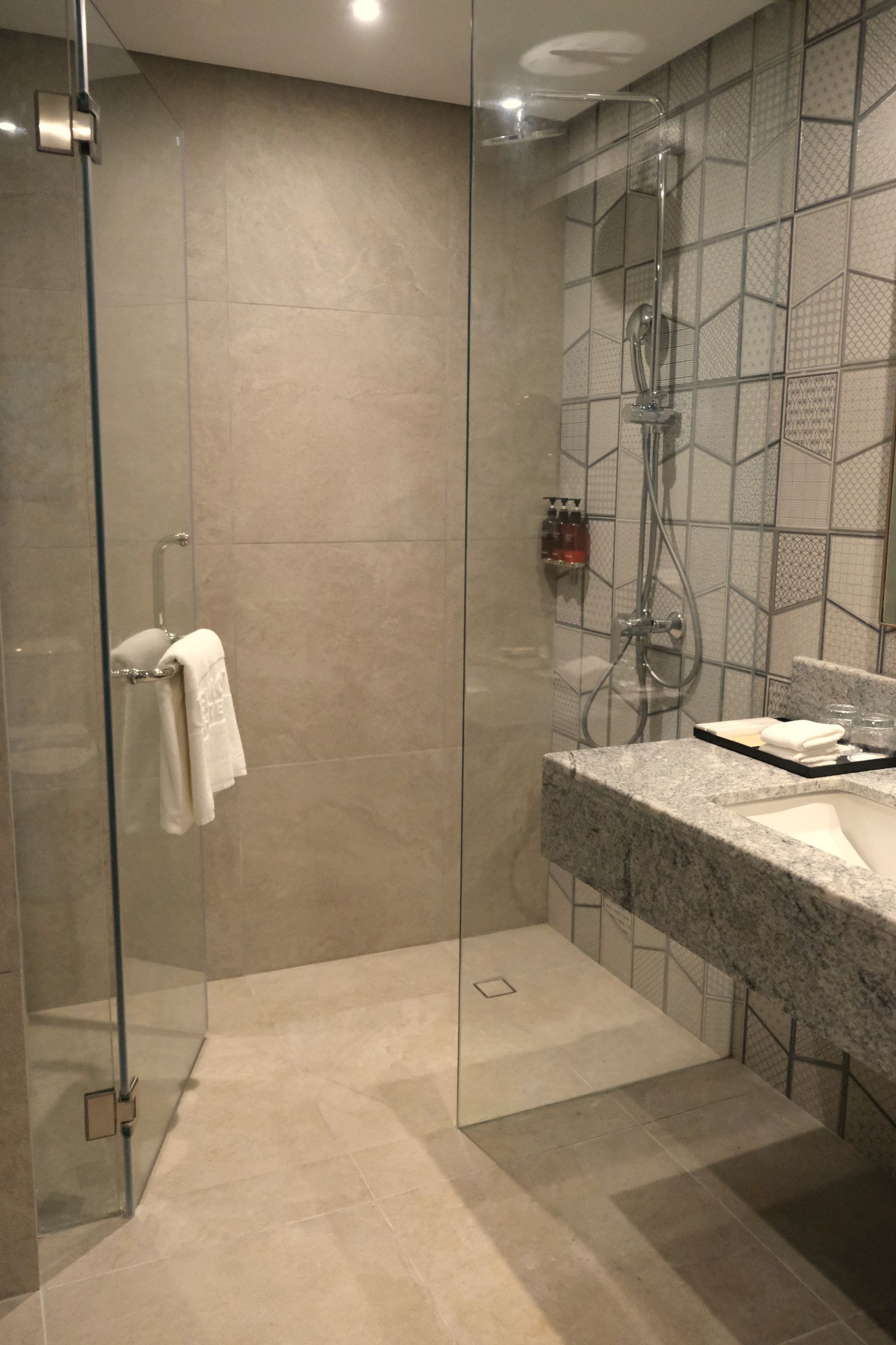 Un baño moderno con ducha envuelta en vidrio, encimera de granito y salpicadero de azulejos.