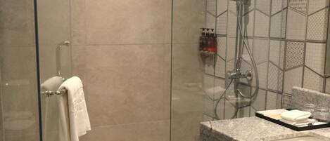 A modern bathroom with a glass-enclosed shower, a granite countertop, and a tiled backsplash.