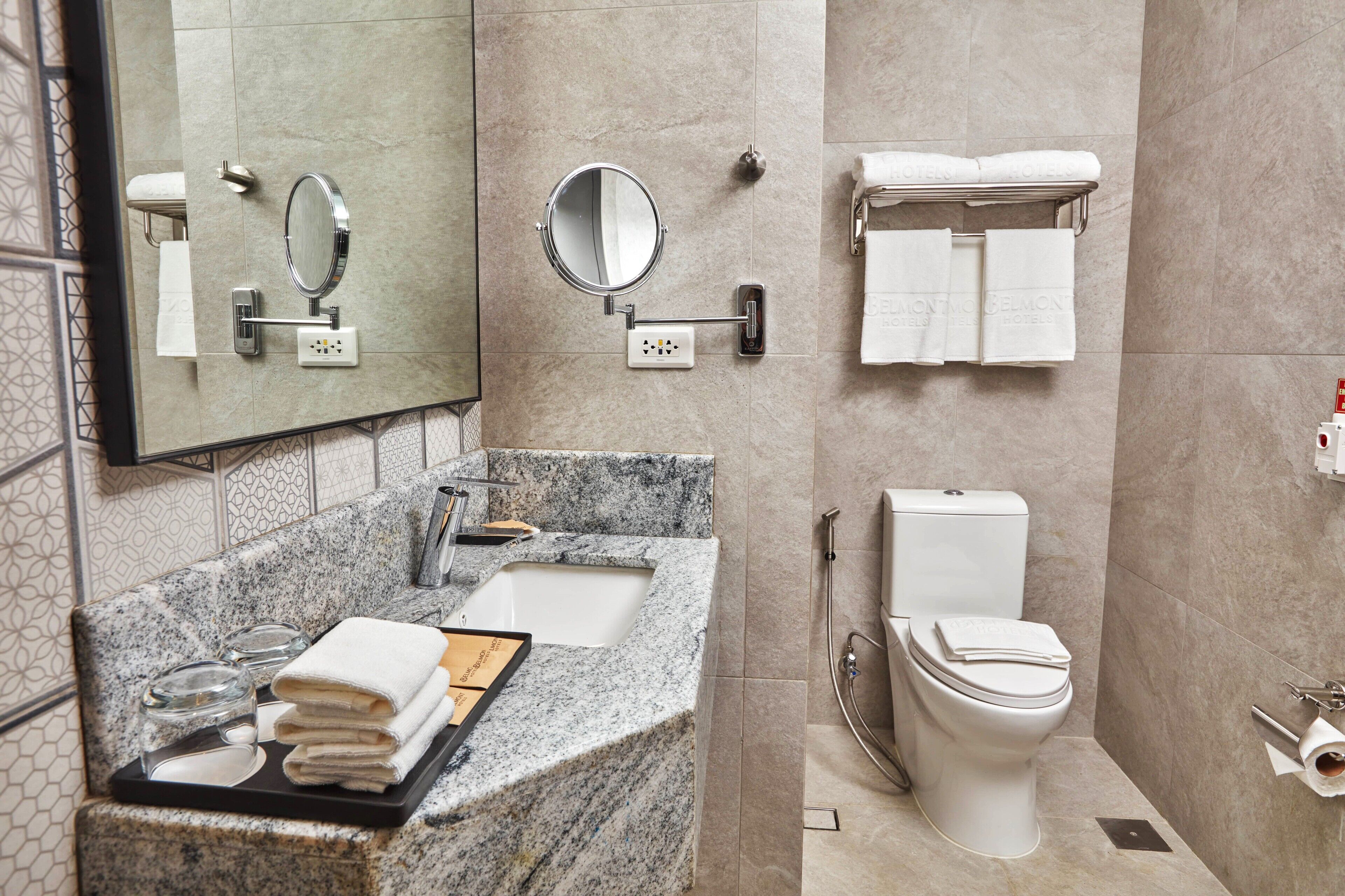 A modern bathroom with a granite sink, a mirror, a toilet, and a towel rack.