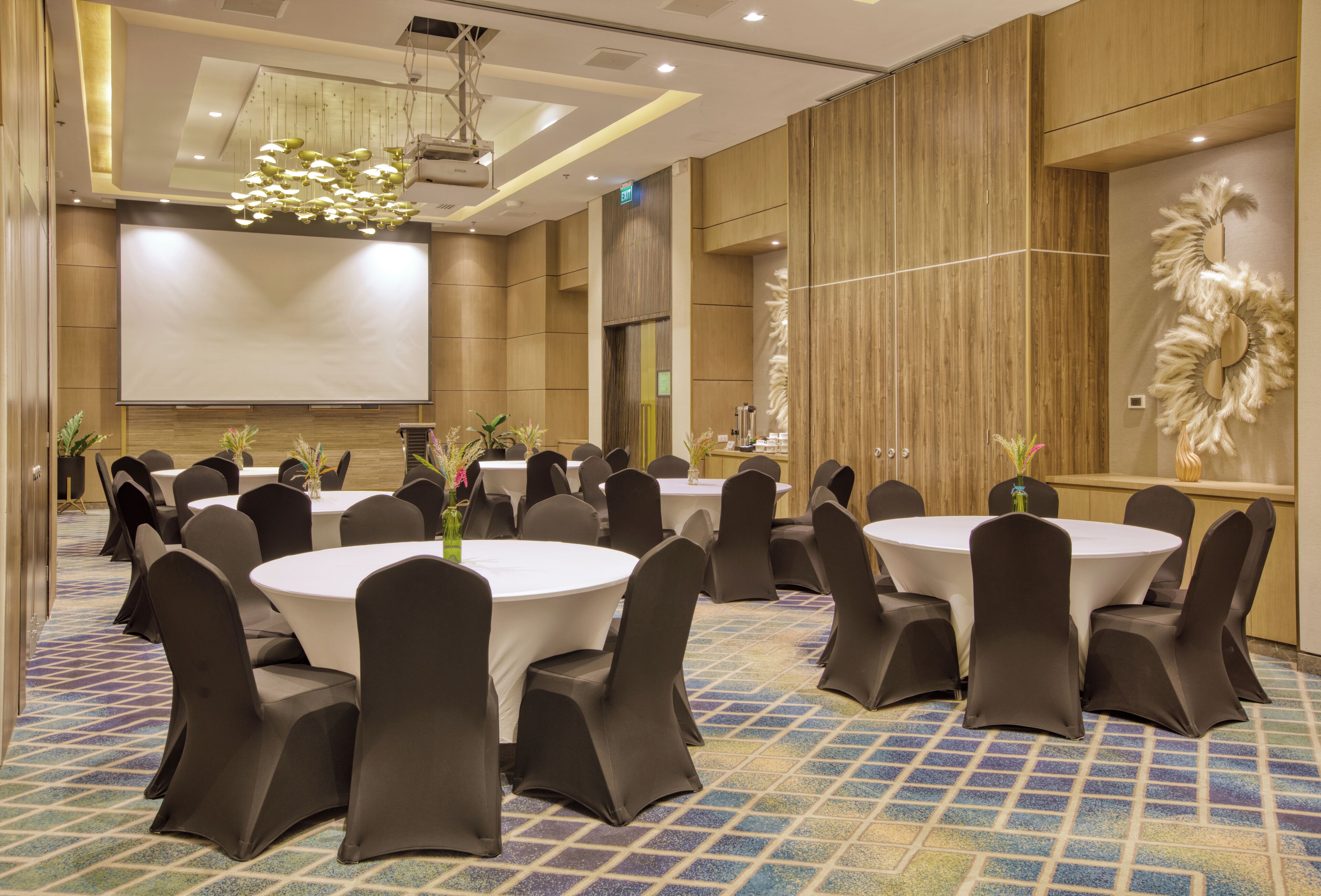 A conference room with round tables and chairs, a projector screen, and a decorative wall.