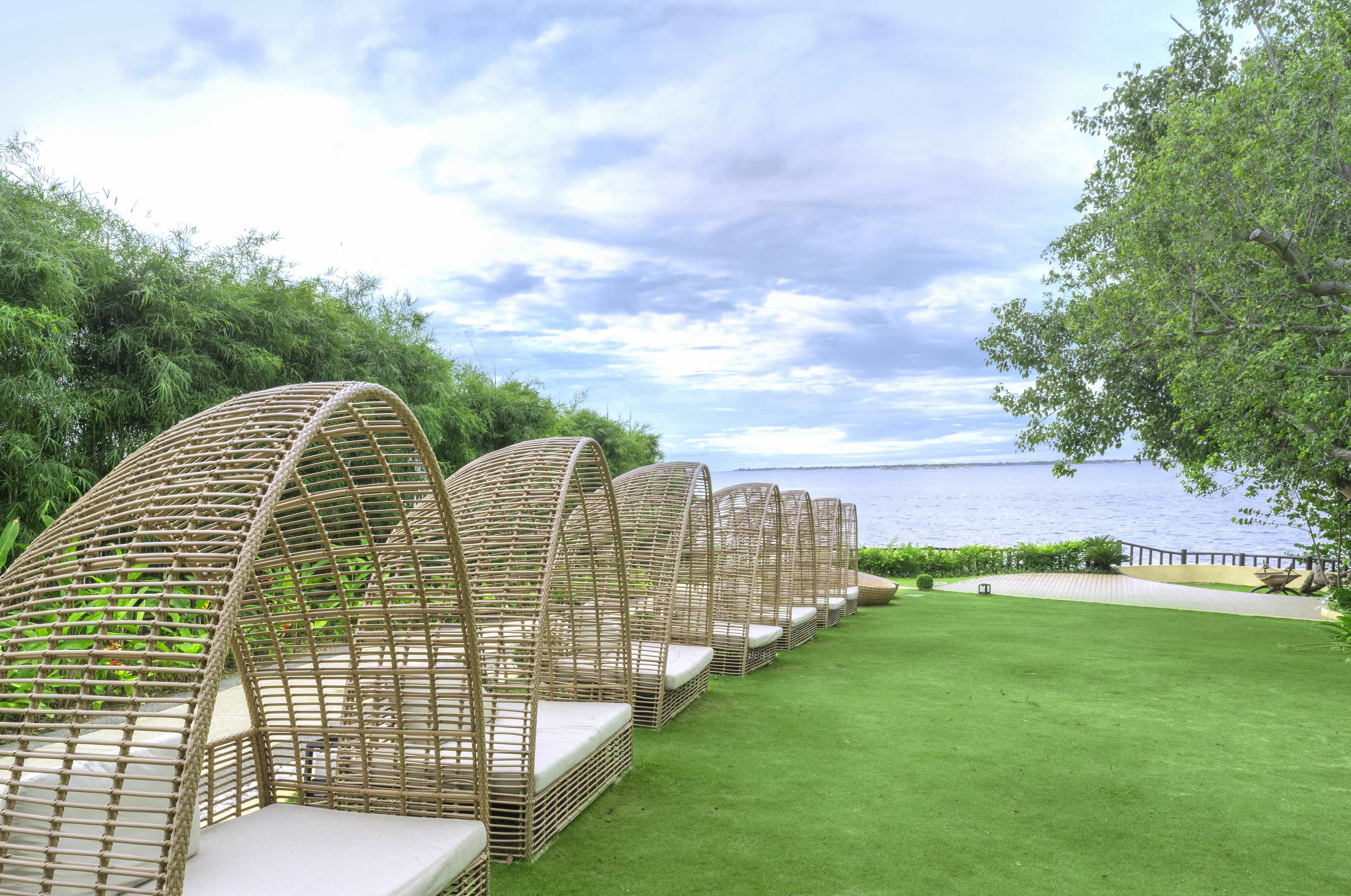 Outdoor wicker furniture arranged on a grassy area with a view of the sea.