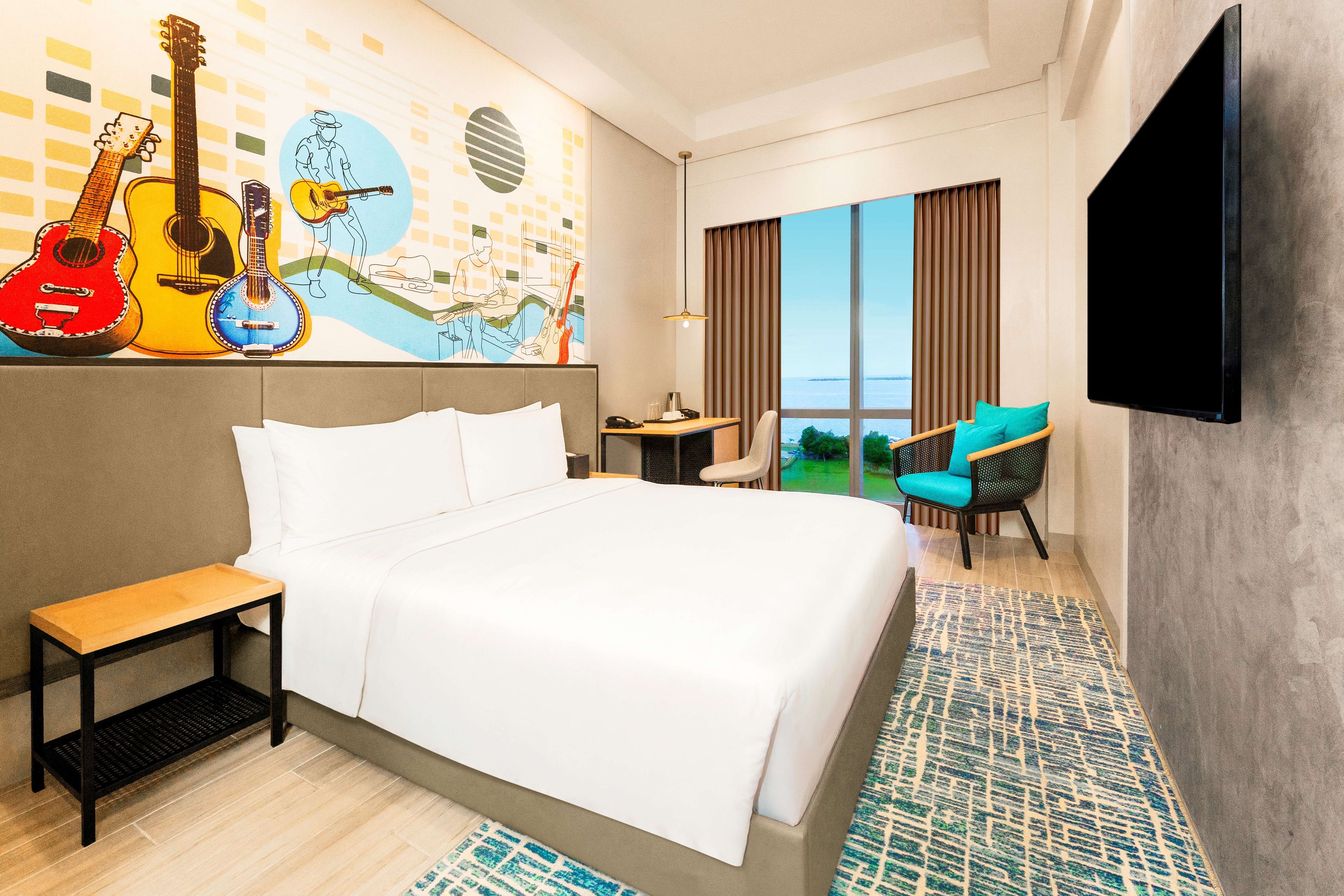 A hotel room with a large bed, a desk, a chair, a TV, and a view of the outdoors.