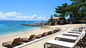 Un resort frente a la playa con sillones de descanso y un edificio de techo de paja.
