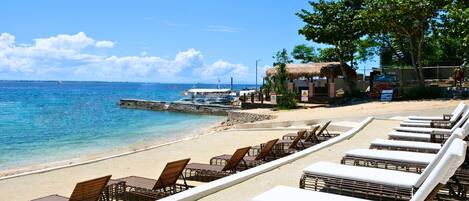 A beachside resort with lounge chairs and a thatched-roof building.