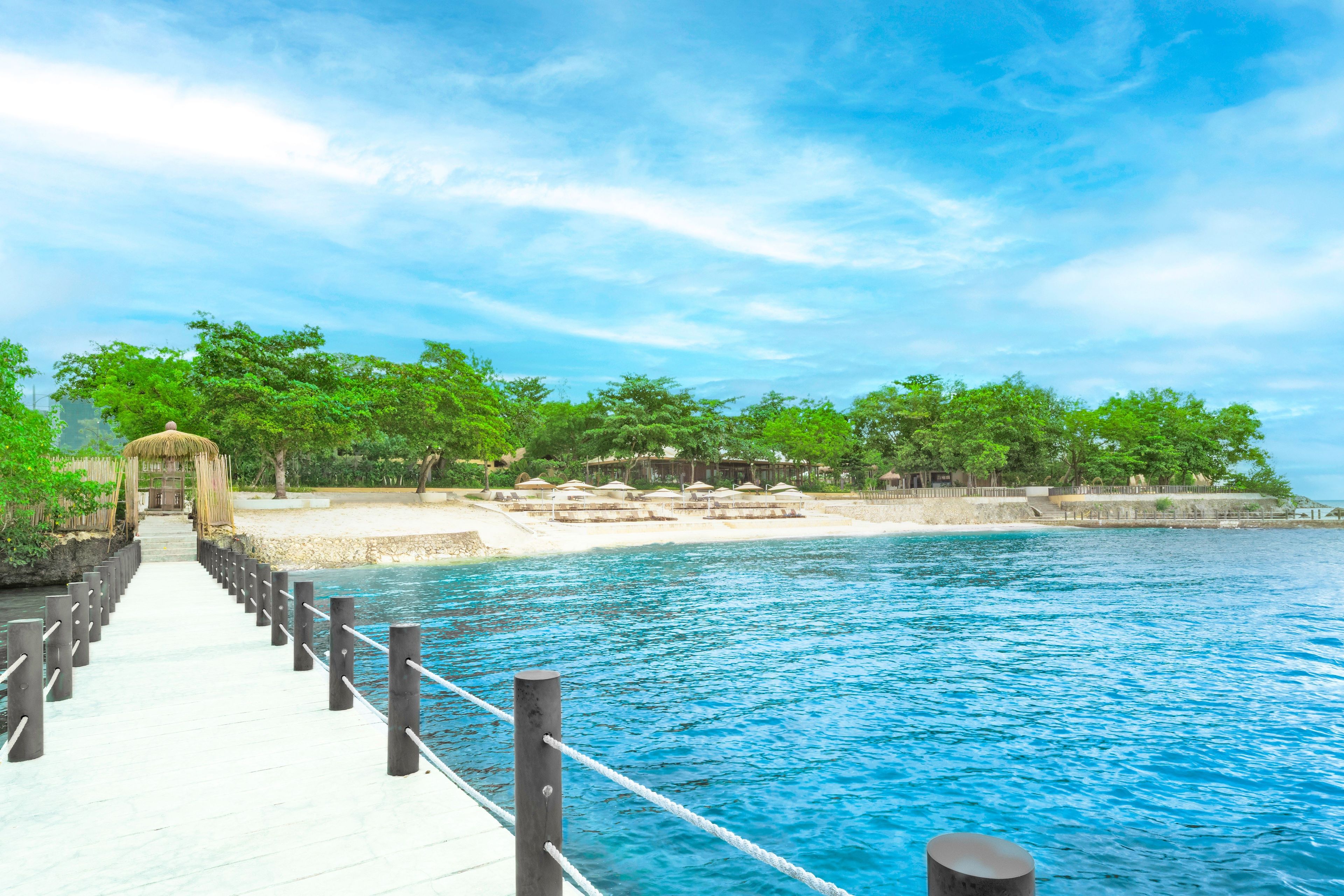 A pier leading to a beach with umbrellas and lounge chairs.