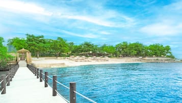 A pier leading to a beach with umbrellas and lounge chairs.