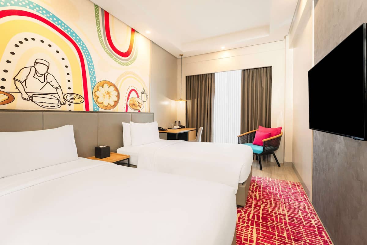 Een hotelkamer met twee bedden, een bureau, een stoel, een televisie en een muur met een kleurrijke muurschildering.