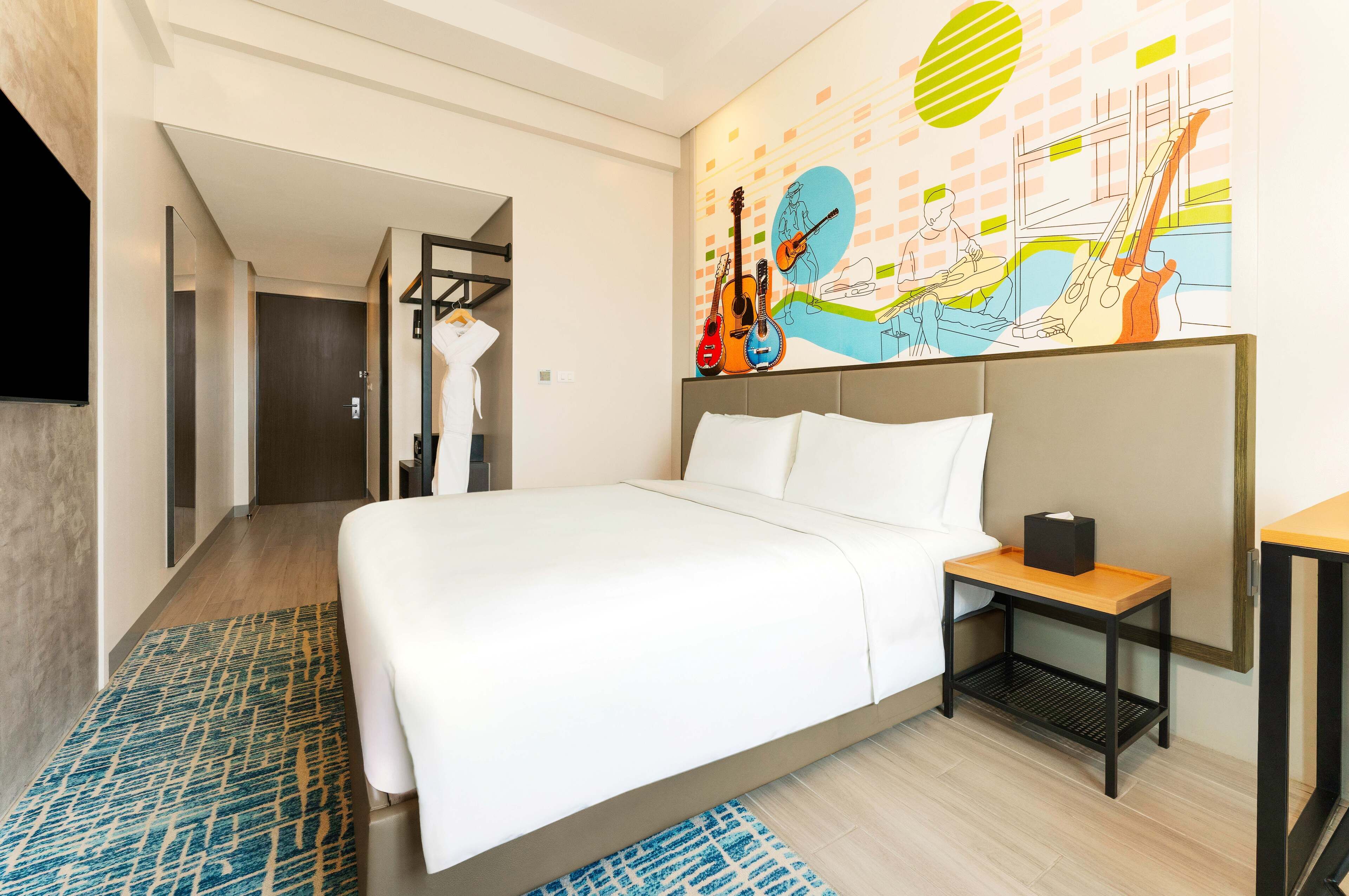 A hotel room with a large bed, a bedside table, a wall-mounted TV, and a colorful mural.