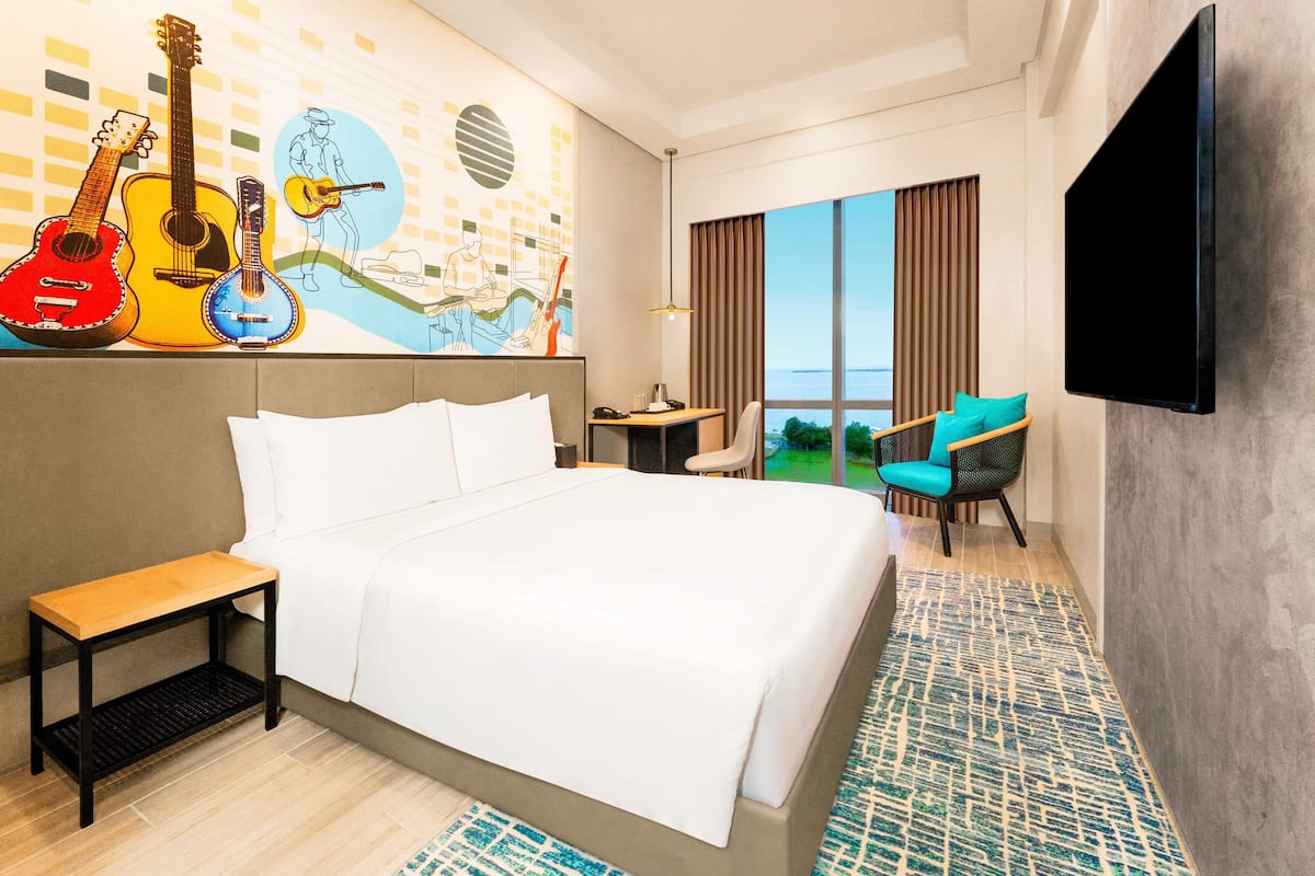 Hotelkamer met een groot bed, een bureau, een stoel, een televisie en een muurschildering van gitaren.