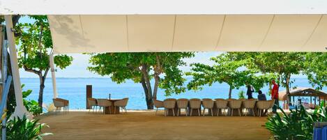 An outdoor seating area with a view of the sea, surrounded by trees and covered by a canopy.