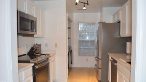 A modern kitchen with white cabinetry, stainless steel appliances, and a window with blinds.