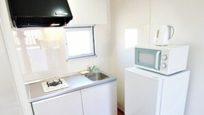 Una cocina compacta con muebles blancos, microondas, cafetera y ventana sobre el fregadero.
