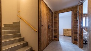 A staircase with a wooden handrail, a wooden door, and a tiled floor leading to a bedroom with a bed and a dresser.