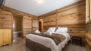 A wooden-paneled bedroom with a bed, a bedside table, and a bathroom visible through an open door.