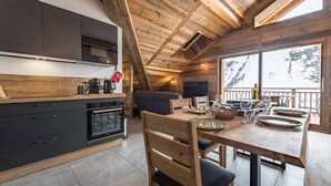 A modern kitchen with dark cabinets, a wooden dining table set for four, and a large window overlooking a snowy landscape.