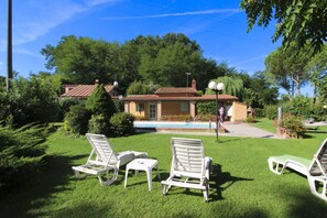 A villa with a swimming pool, surrounded by lush greenery and white lounge chairs.