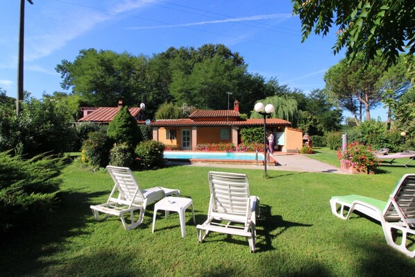 Una casa con piscina, rodeada de vegetación y sillones blancos.