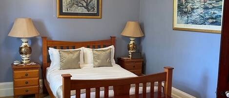 Quarto com cama de madeira, duas mesas de cabeceira com abajures, um lustre e duas pinturas emolduradas nas paredes.