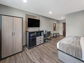 Habitación de hotel con cama, escritorio con silla, televisión, minibar y armario.