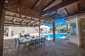 Un área de comedor al aire libre con piscina y sillones de descanso.