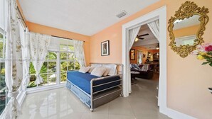 Une chambre à coucher avec un lit, une fenêtre avec des rideaux, un miroir et une porte donnant sur une autre pièce.