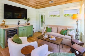 Un salon chaleureux avec un canapé, des fauteuils, une table basse, un téléviseur fixé au-dessus d’un meuble en bois et une fenêtre donnant sur un paysage verdoyant.